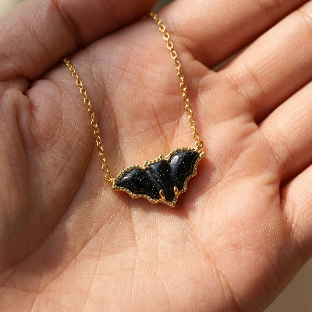 The Kendra Scott golden obsidian bat short pendant necklace placed in a palm for size and scale reference.