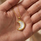 The Kendra Scott white mother of pearl crescent moon necklace placed in a hand for scale and texture reference.