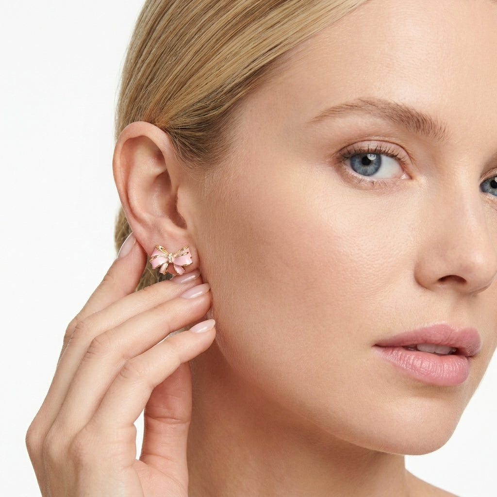 Blonde female model wearing the Kendra Scott x LoveShackFancy pink and gold bow stud earrings.
