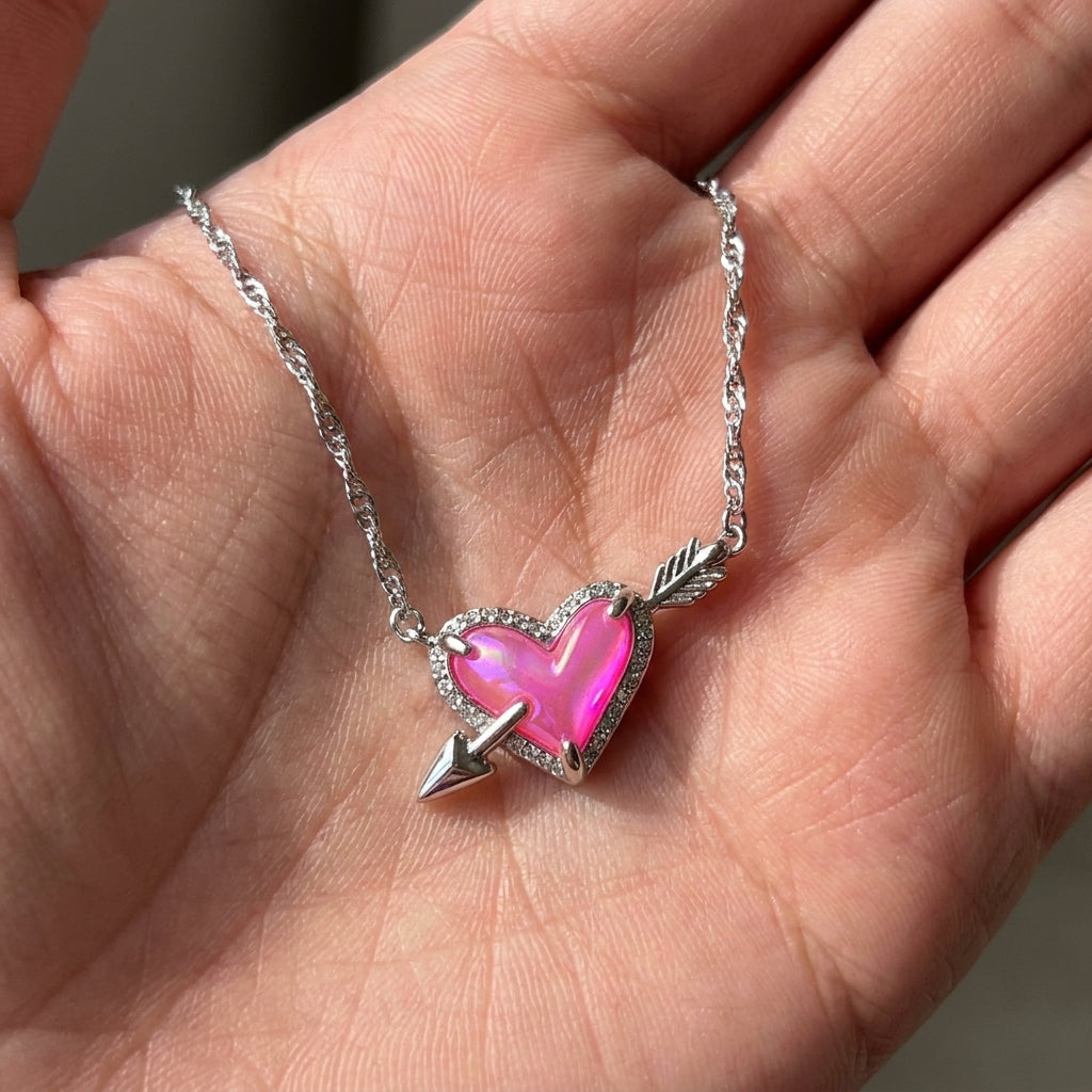 Close-up of a hand holding the silver Kendra Scott Ari heart necklace to show vibrant pink light reflection.