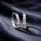 Pair of lab grown diamond X cross cable wire huggie earrings resting on dark blue silk.