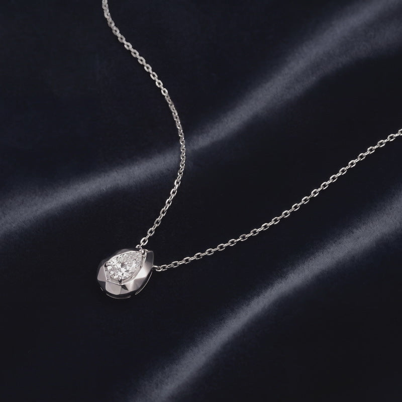 Pear cut lab grown diamond faceted bezel pendant resting on dark navy silk fabric.