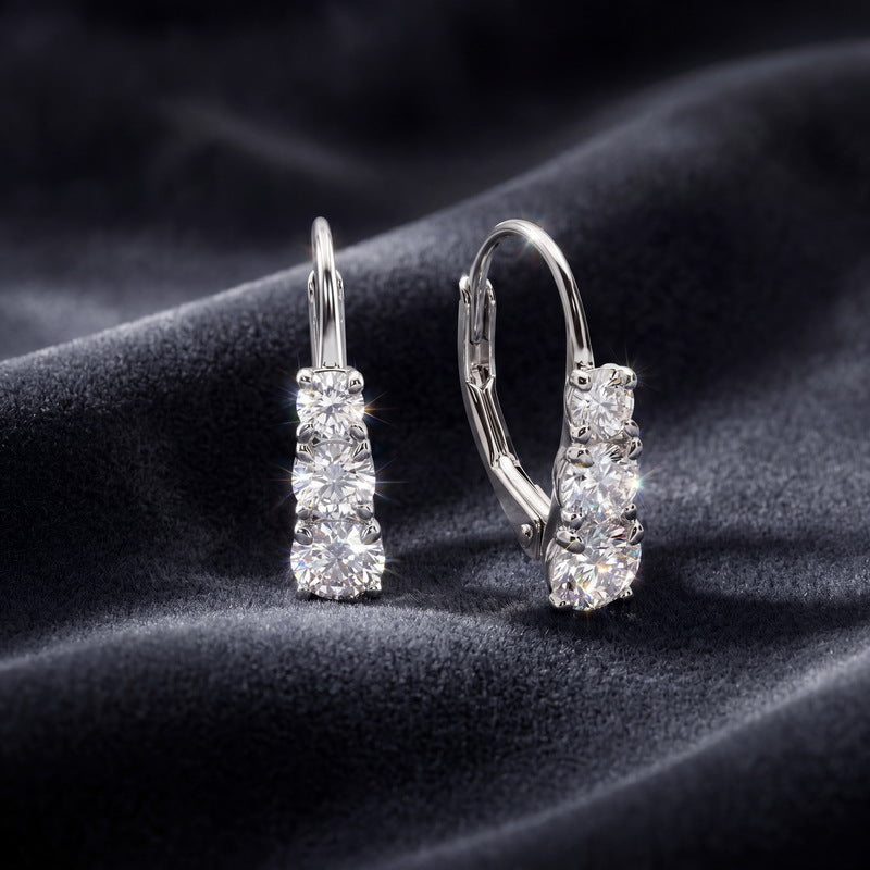 Pair of lab grown diamond three stone leverback earrings resting on dark navy silk.