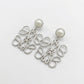 Macro detail of the silver Anagram earrings showing the smooth metal luster and pearl nacre