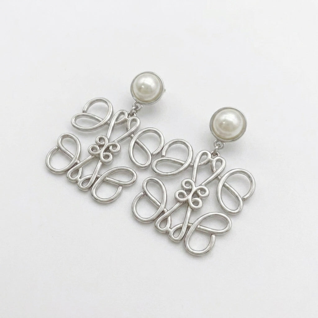 Macro detail of the silver Anagram earrings showing the smooth metal luster and pearl nacre