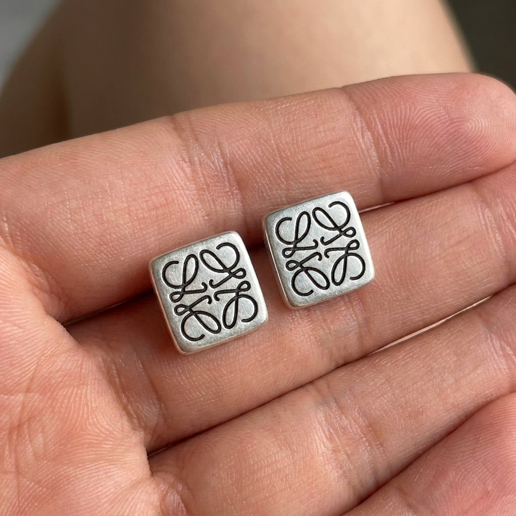 Hand-held size reference of the Loewe Silver Square Studs to show the delicate scale