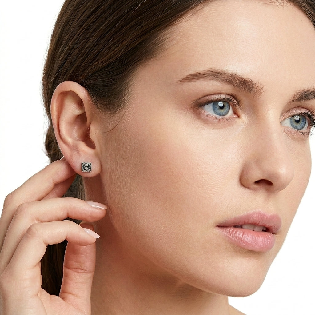 Model touches hair wearing Loewe Silver Anagram Square Studs, capturing the metallic glow