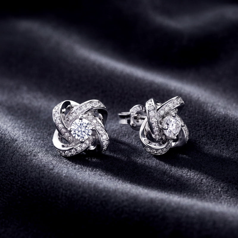 Angled profile view of love knot round lab diamond pavé halo stud earrings on dark silk.