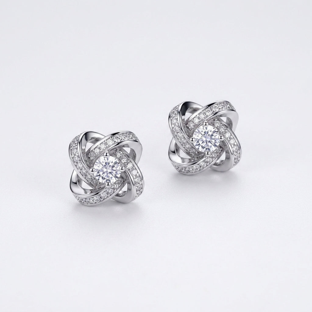 Pair of love knot round lab diamond pavé halo stud earrings on white background.