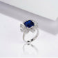 Close-up lifestyle view of a moody model leaning on her hand, displaying an elegant blue sapphire sunflower halo engagement ring.