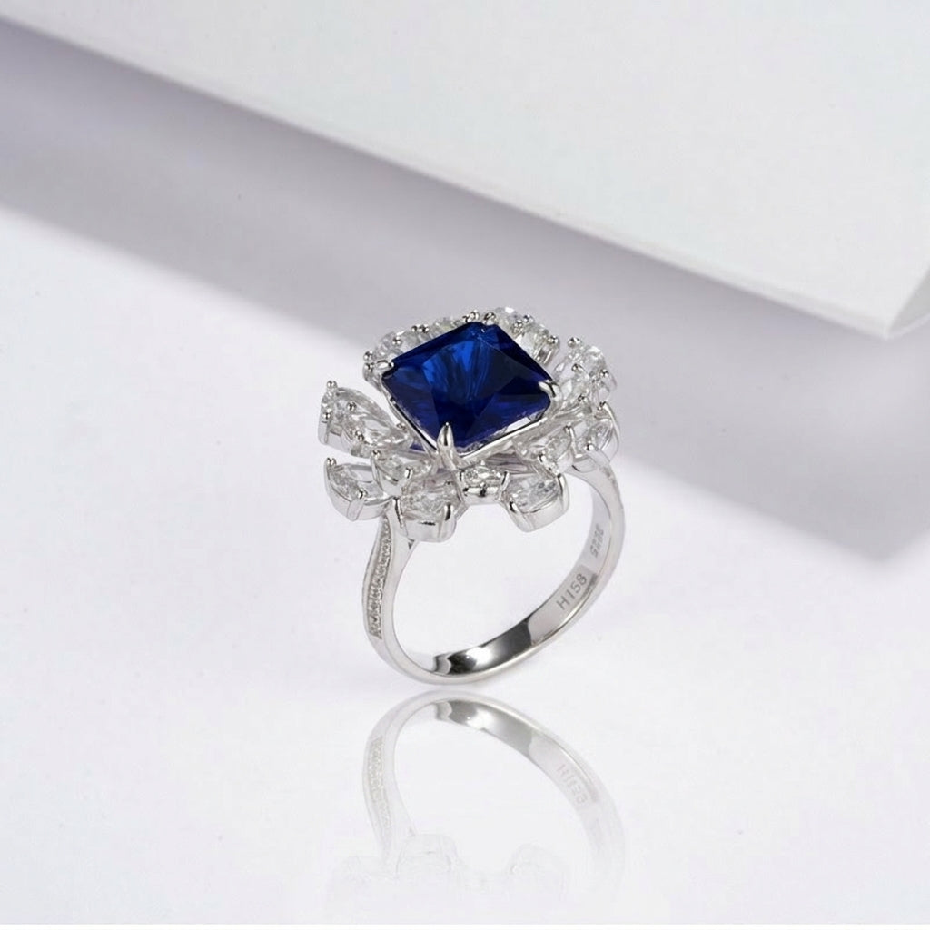 Close-up lifestyle view of a moody model leaning on her hand, displaying an elegant blue sapphire sunflower halo engagement ring.