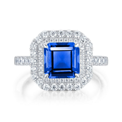 White background front view showcasing a luxury emerald-cut blue sapphire double halo statement ring with a pave diamond band.