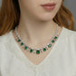 Elegant model smiling and gesturing toward her cushion-cut emerald fringe necklace, lifestyle view.