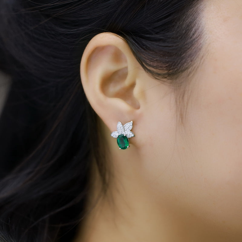 Side view of a model wearing the short stud side of luxury oval-cut emerald asymmetric leaf earrings.