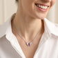 Lifestyle chest shot of a smiling model wearing a luxury pave diamond butterfly necklace with a red marquise ruby centerpiece.