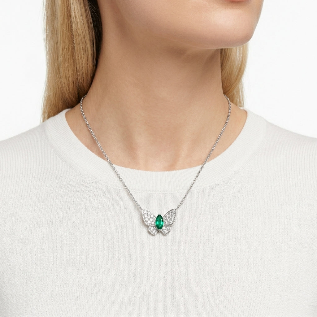 Lifestyle chest shot of a model wearing a luxury pave diamond butterfly necklace with a green marquise emerald centerpiece.