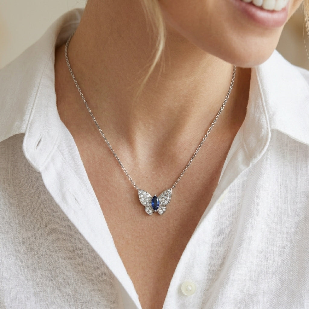 Lifestyle chest shot of a blonde model wearing a luxury pave diamond butterfly necklace with a royal blue sapphire center.