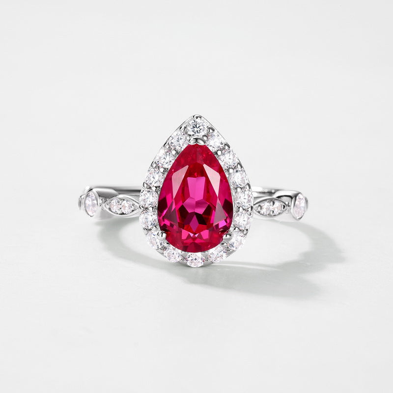 White background front view showcasing a luxury pear-shaped lab-grown ruby halo engagement ring with a pave diamond band.