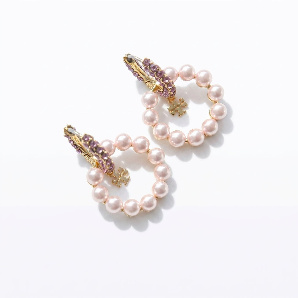 High-angle studio view of luxury pearl circle hoop earrings with shimmering crystal hugging posts and dangling logo charms.