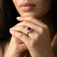 Close-up editorial portrait of a model holding her chin, displaying a luxury emerald-cut ruby statement double halo ring.