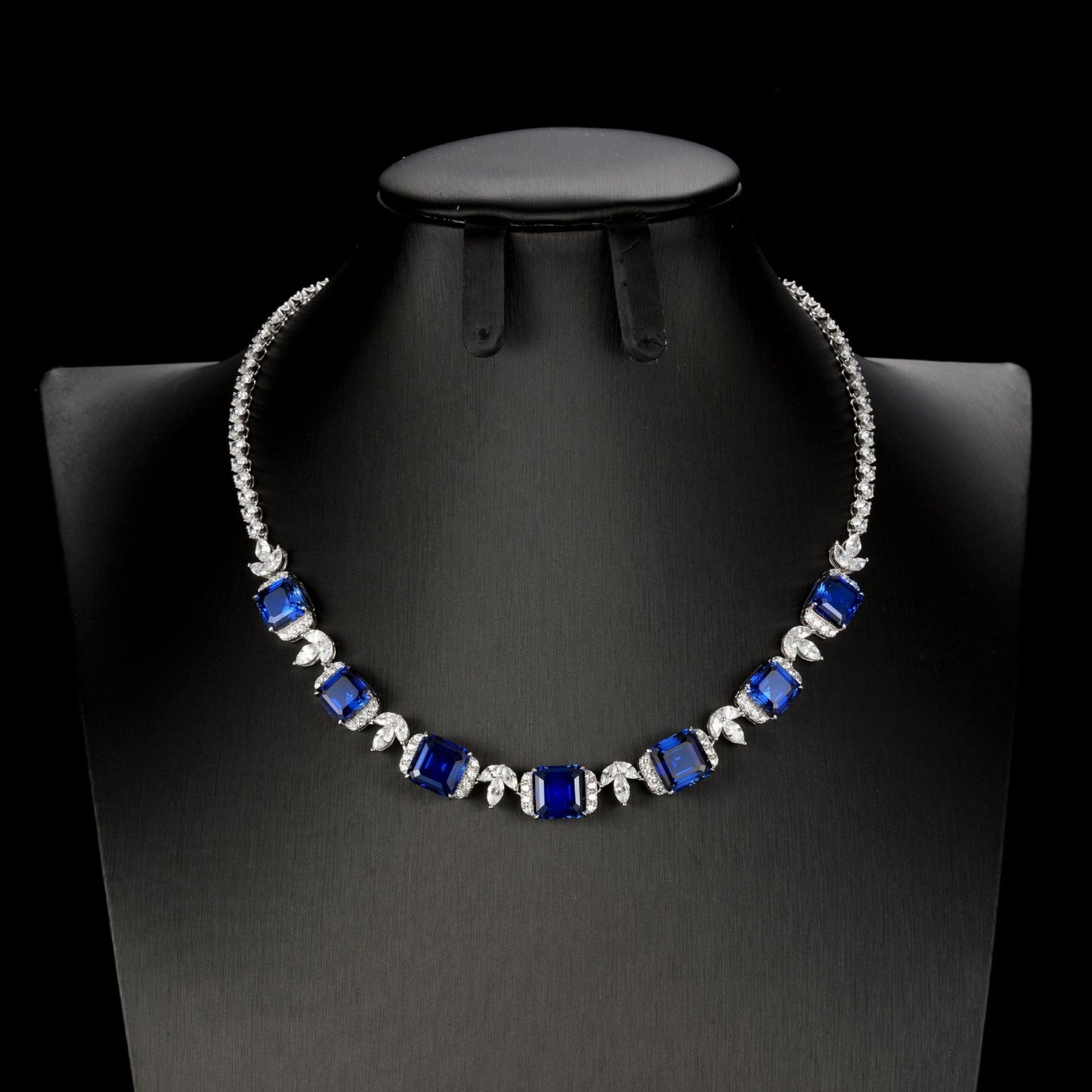 Front product view of a luxury square-cut blue sapphire statement necklace displayed on a premium black mannequin bust.