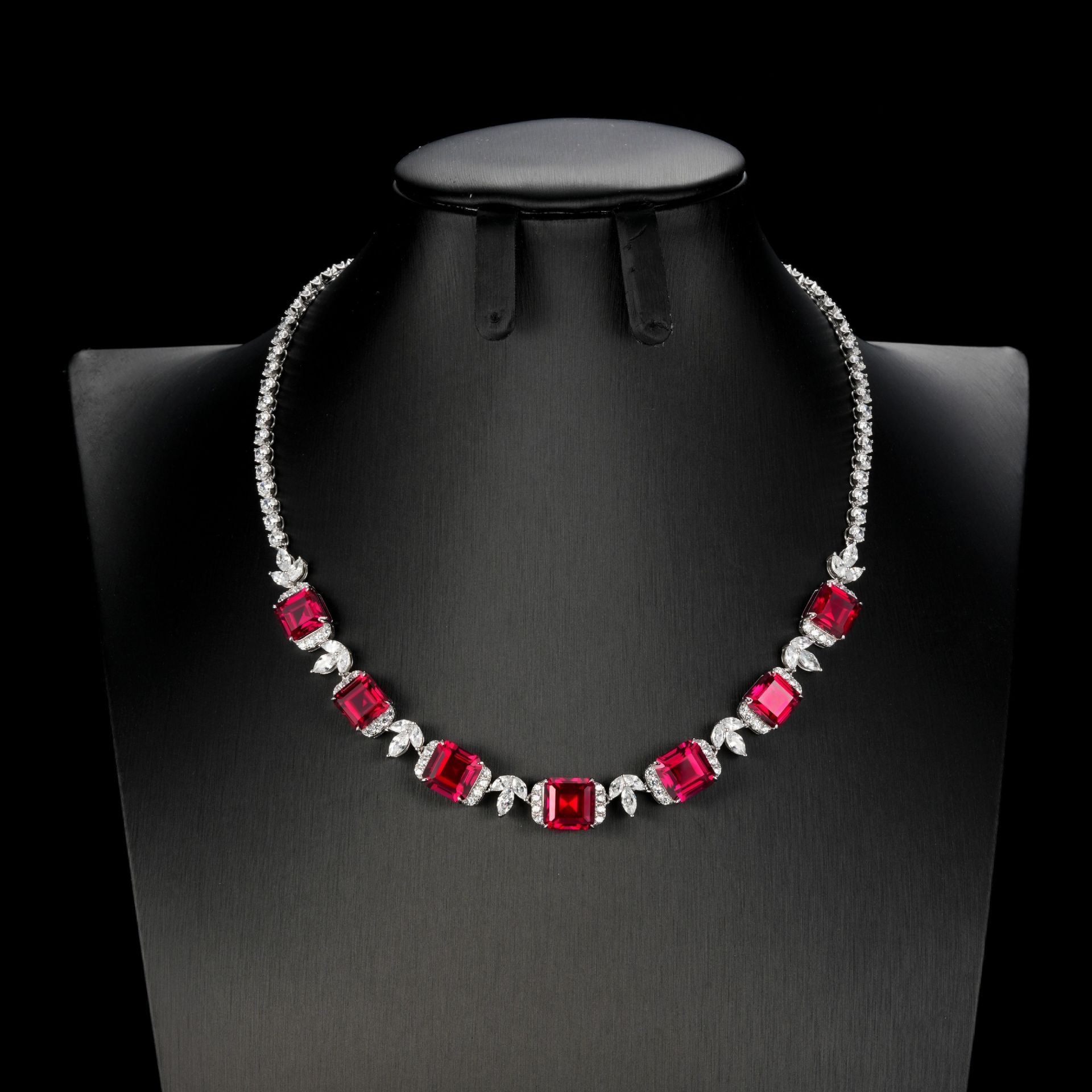 Front product view of a luxury square-cut ruby statement necklace displayed on a premium black mannequin bust.