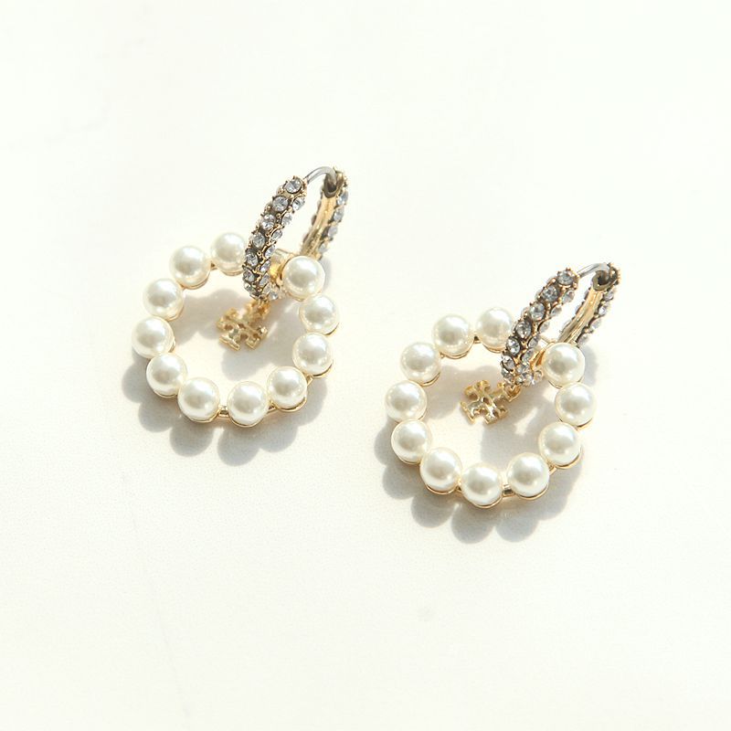 High-angle studio view of luxury white pearl circle earrings featuring shimmering crystal huggie posts and dangling logo charms.