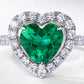 Macro close-up shot capturing the vivid green clarity, step-cut facets, and micro pave diamond halo of the heart emerald ring.