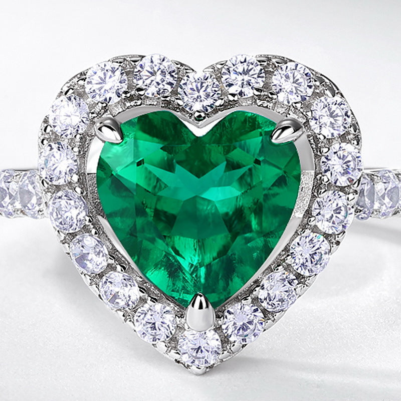 Macro close-up shot capturing the vivid green clarity, step-cut facets, and micro pave diamond halo of the heart emerald ring.