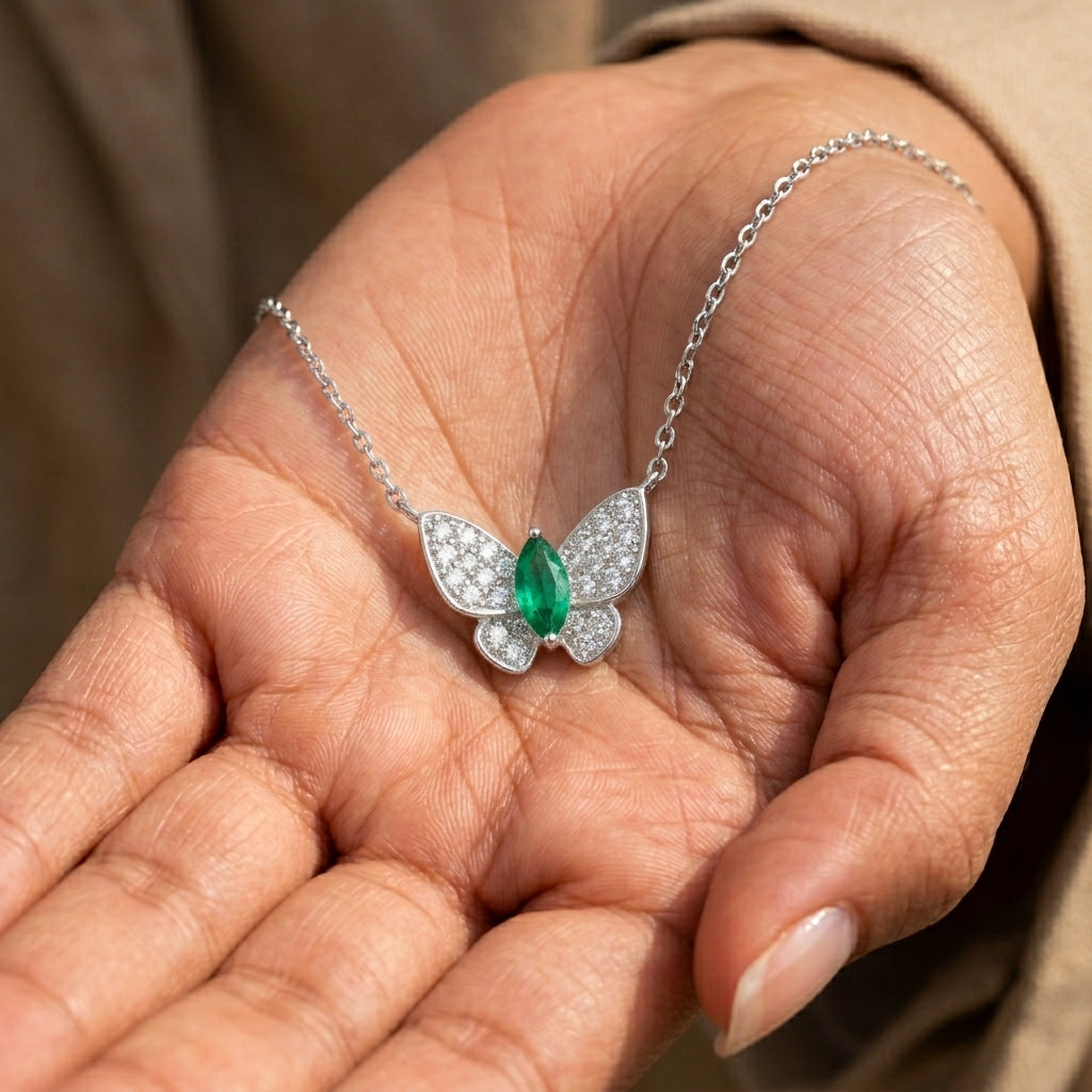 Real-life lifestyle hand view of a model holding a luxury marquise-cut emerald butterfly pendant necklace in her palm.