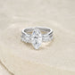 Marquise moissanite three stone ring with contoured paved band resting on textured surface.