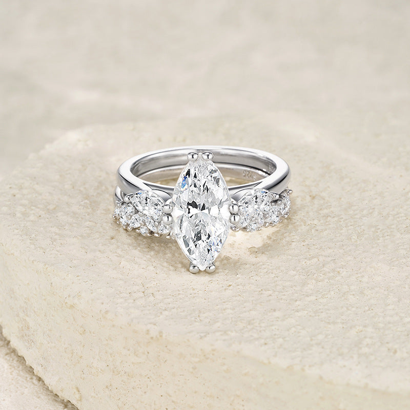 Marquise moissanite three stone ring with contoured paved band resting on textured surface.