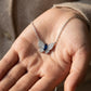 Real-life lifestyle hand view of a model holding a luxury marquise-cut sapphire butterfly pendant necklace in her palm.