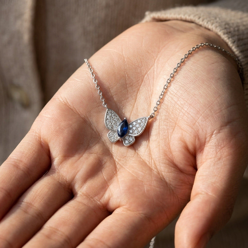 Real-life lifestyle hand view of a model holding a luxury marquise-cut sapphire butterfly pendant necklace in her palm.