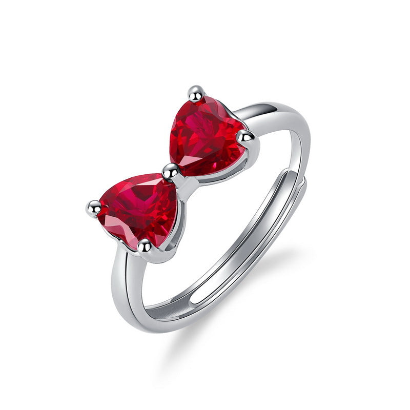 White background profile view of a minimalist ruby heart bow-knot adjustable open ring showcasing the split band.