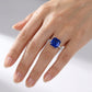 High-angle view of a luxury minimalist square blue sapphire cocktail ring styled on a woman's finger.