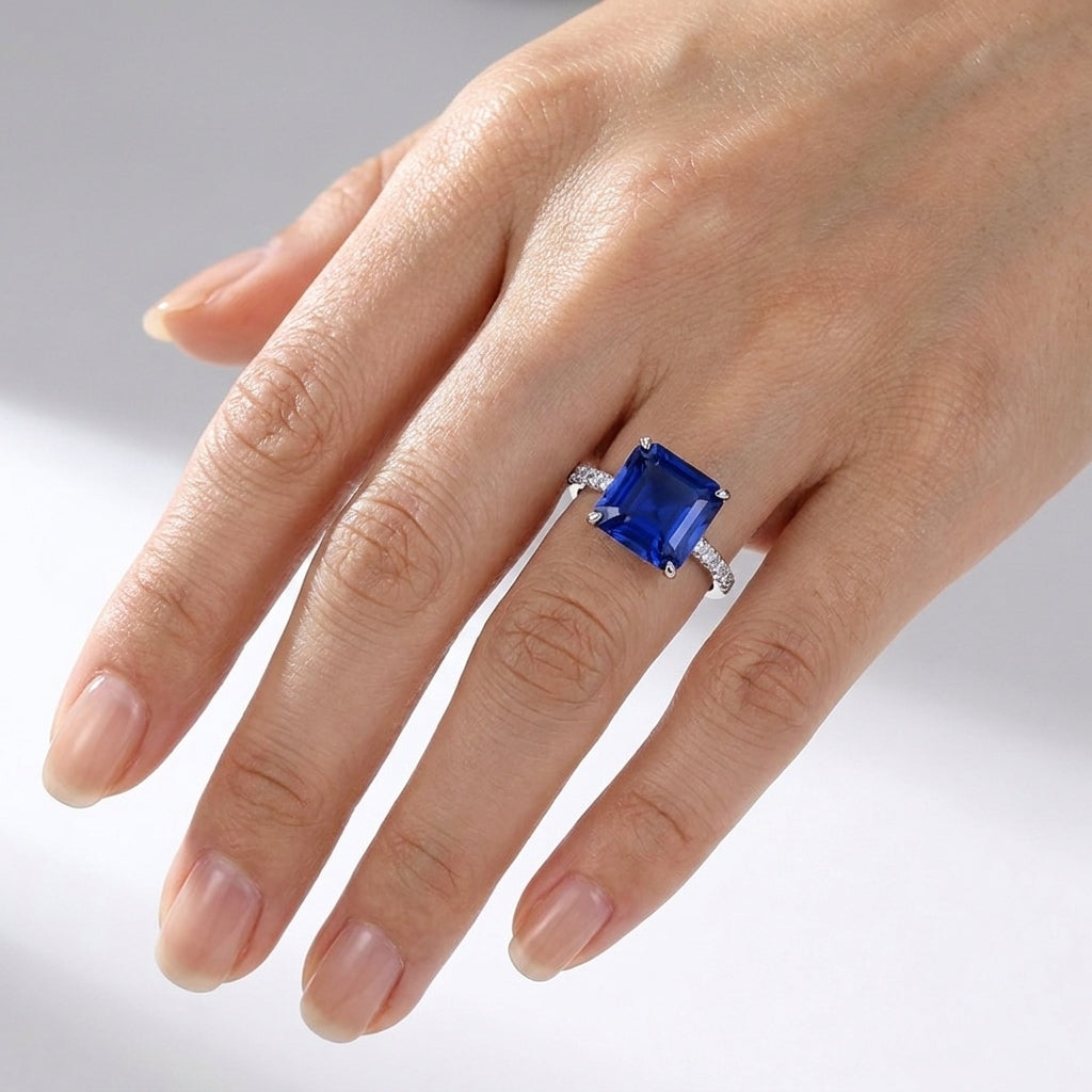 High-angle view of a luxury minimalist square blue sapphire cocktail ring styled on a woman's finger.