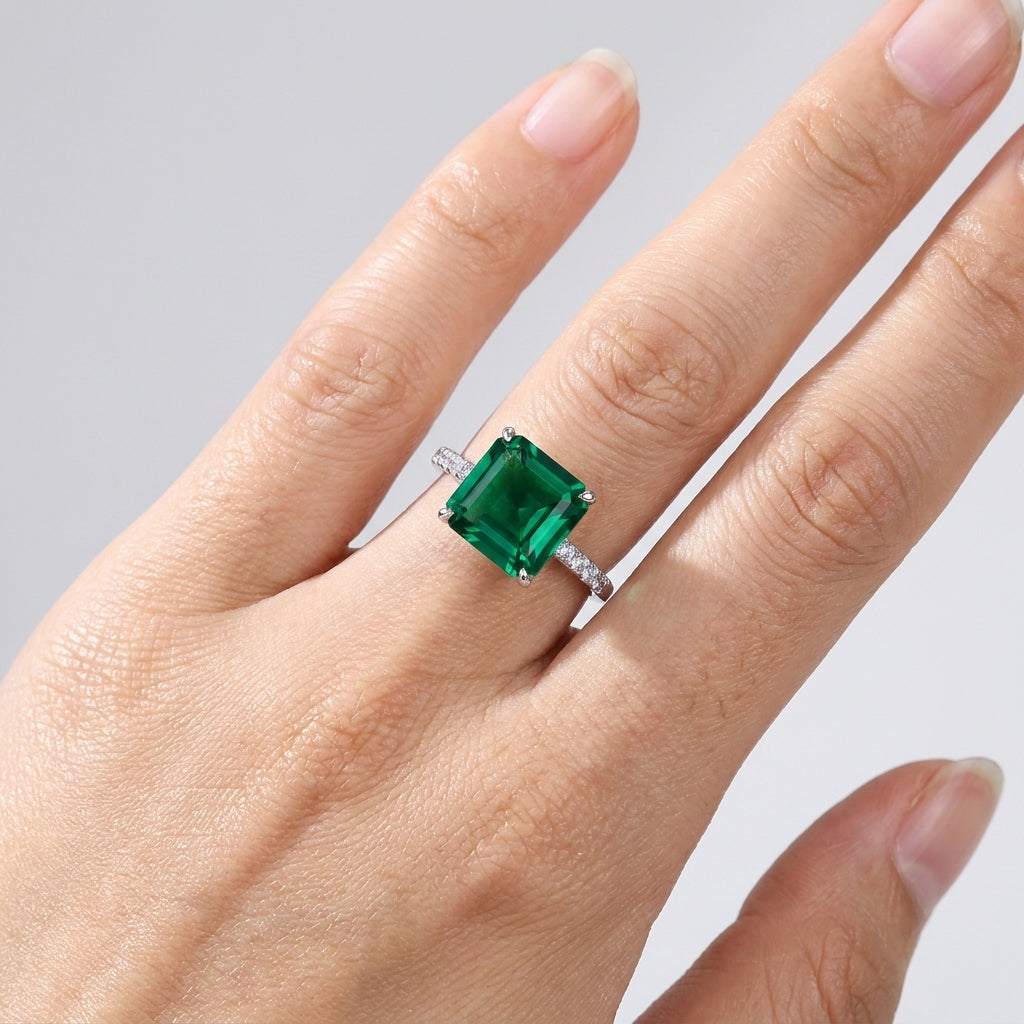 Hand wearing a ring with a green gemstone on a neutral background