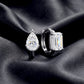 Pair of mismatched pear and emerald cut lab diamond bezel huggie hoops resting on dark silk fabric.