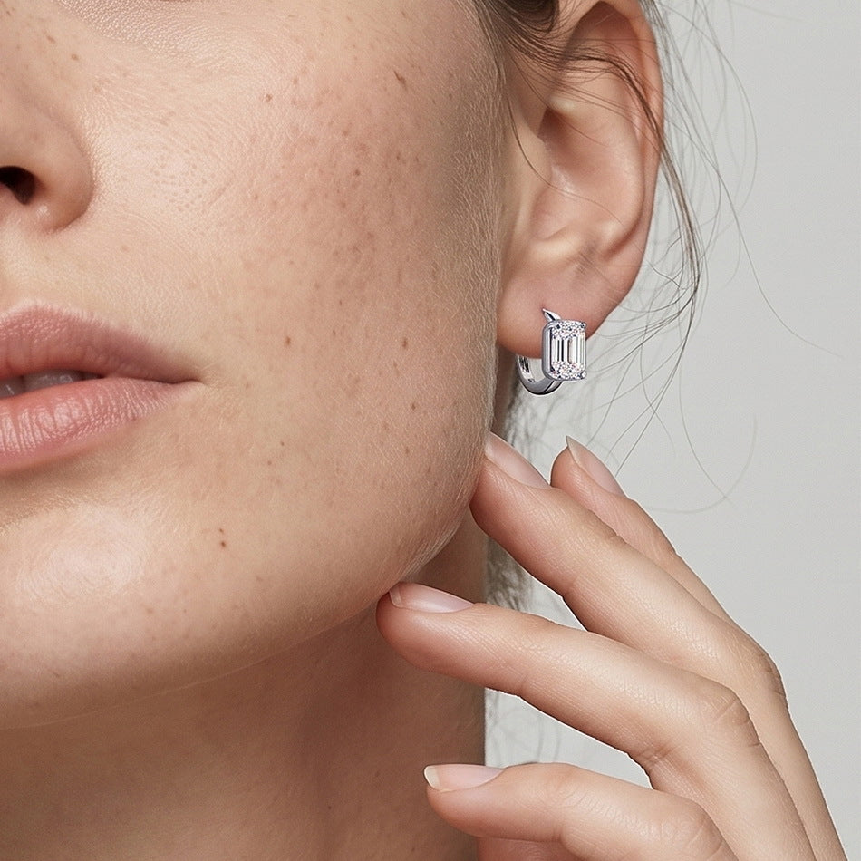 Close-up shot of model ear wearing asymmetrical emerald cut bezel huggie hoop earring.