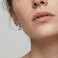 Model wearing mismatched pear and emerald cut lab grown diamond bezel huggie hoop earrings.