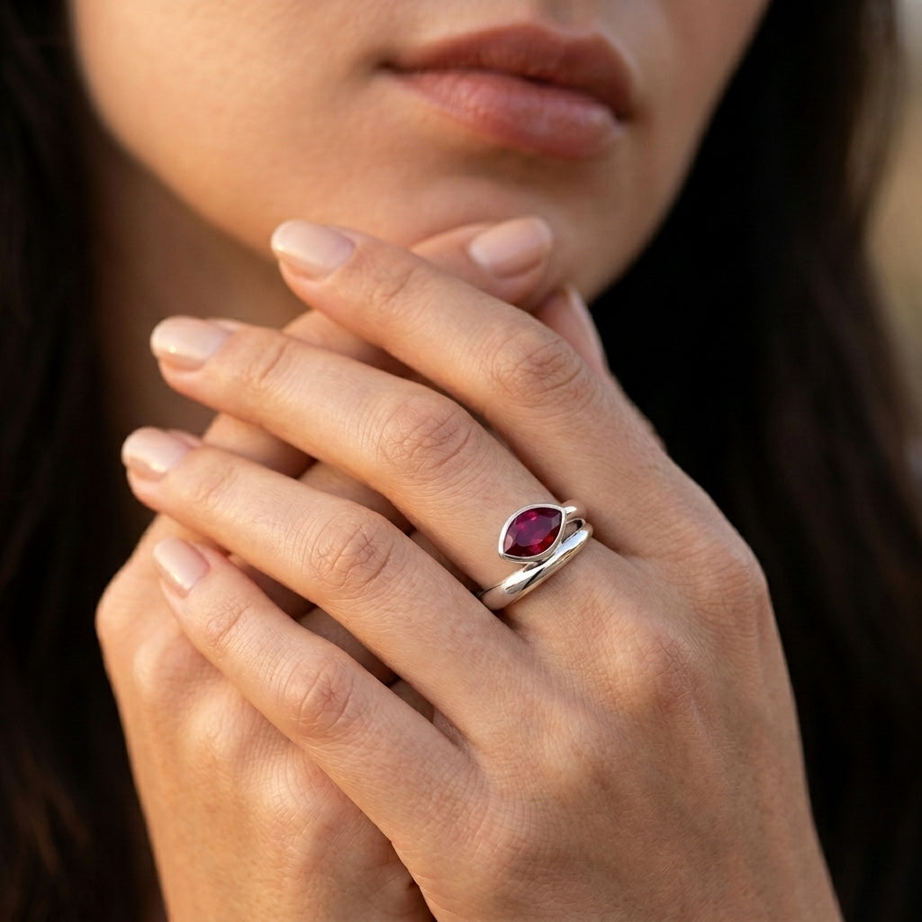 Close-up editorial lifestyle portrait of a model showcasing a modern marquise-cut ruby statement ring on her hand.