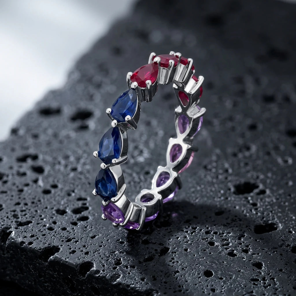 Silver multi-color pear cut rainbow eternity band ring on textured black volcanic stone surface
