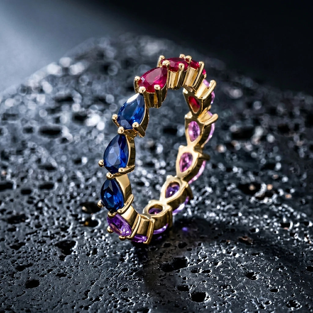 Gold multi-color pear cut rainbow eternity band ring on textured dark stone surface with lighting effects