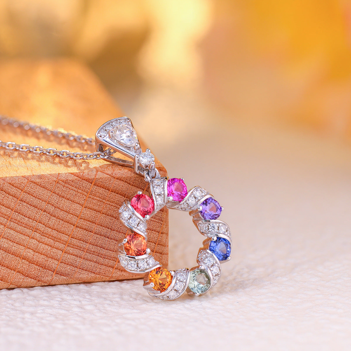 Close-up angled view showing pave ribbon detail of multi-color sapphire wreath pendant.