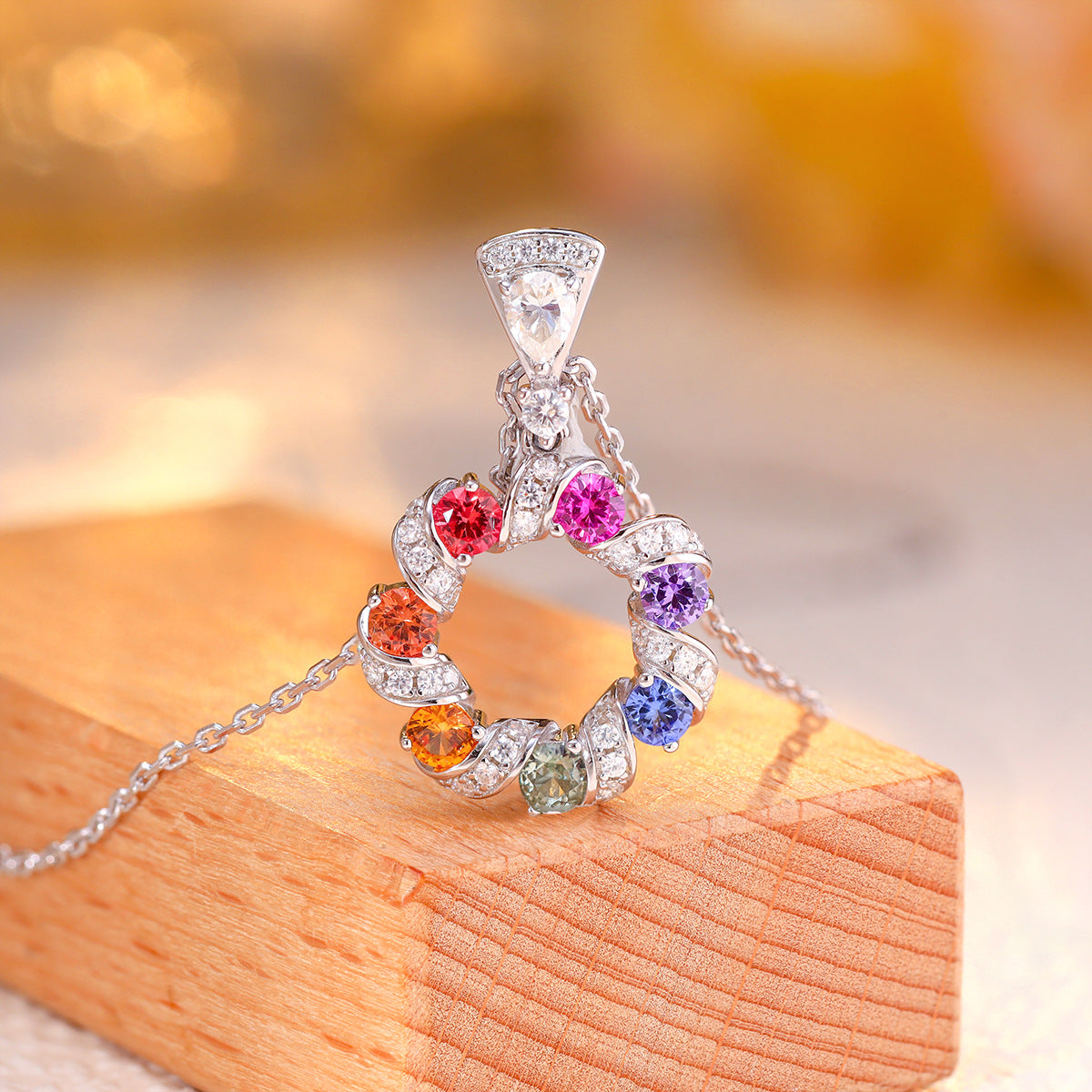 Side perspective of multi-color sapphire wreath circle pendant resting on wooden display stage.