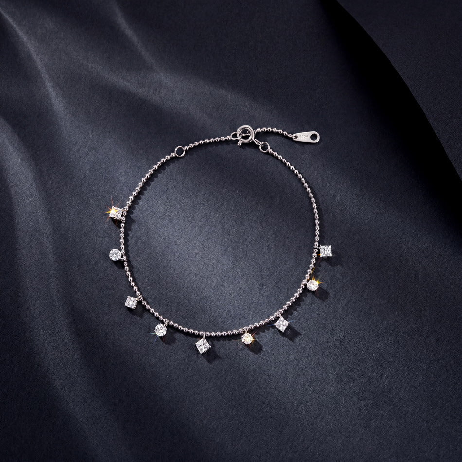 Circular view of multi-shape dangle station bead chain bracelet on dark silk.