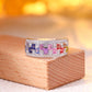 Side view of multicolor baguette gemstone and moissanite wide band ring displayed on wooden block