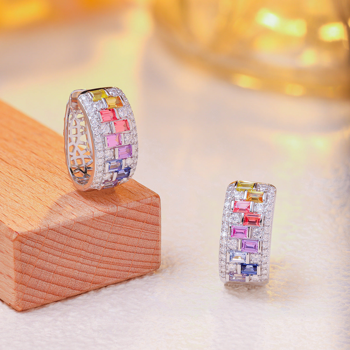 Pair of multicolor baguette gemstone and moissanite wide huggie hoop earrings on wooden display blocks