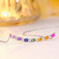 Angled perspective view of multicolor gemstone and moissanite rainbow bar necklace on white surface